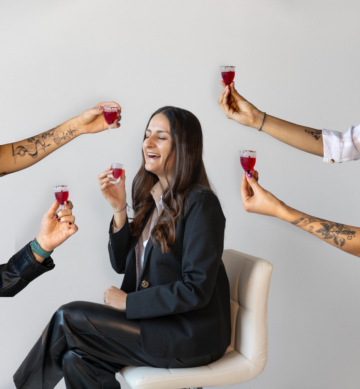 Paula León, founder of Blean, laughing in a black blazer as four friends reach into frame to toast her with small glasses