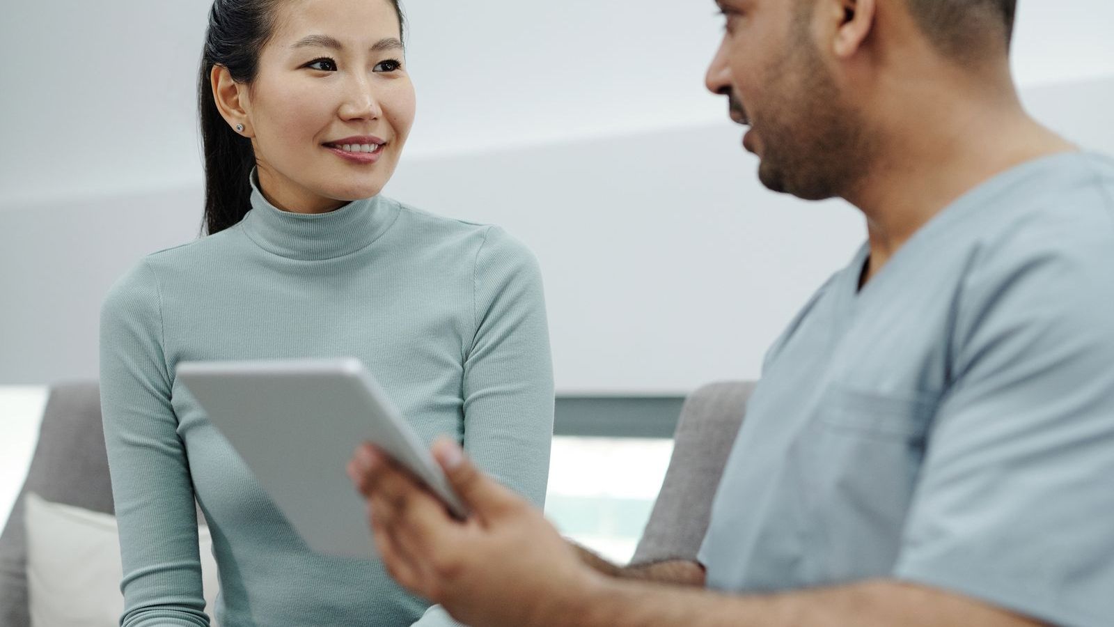 A young woman sitting and talking with a healthcare provider in scrubs in a bright, calm clinic room