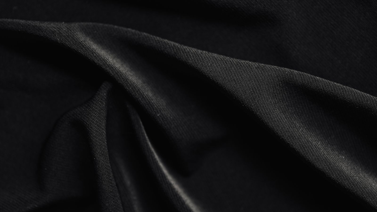 Folded black cotton fabric on a soft neutral surface with gentle light